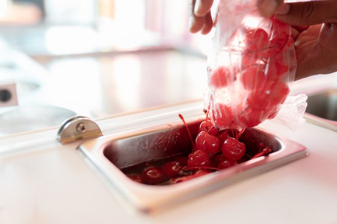 An ice-cream parlor worker is dropping some cherry toppings into the counter tray