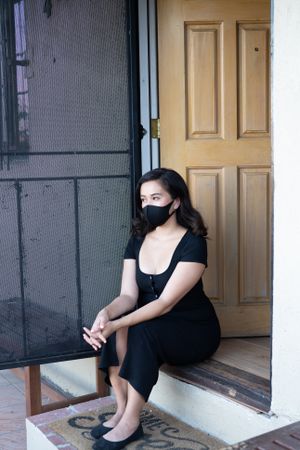 Woman sitting by front door of house with mask