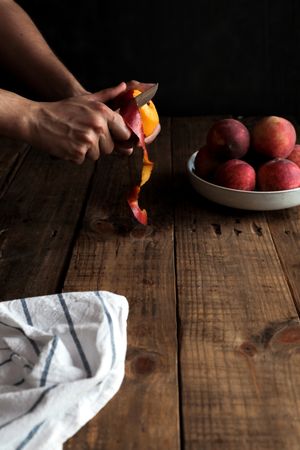 Tasty ripe peaches in plate and hands peeling peach
