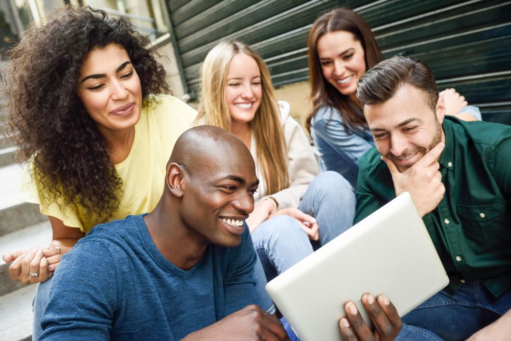 Men and women engaged by something on digital tablet while sitting on outdoor cement staircase