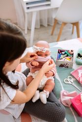 Girl trying on her doll a mask that she is sewing