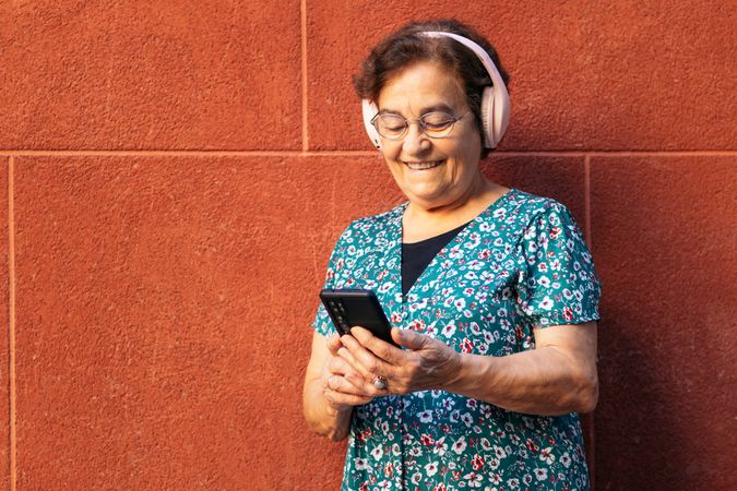 Older woman using smartphone and listening to music with headphones