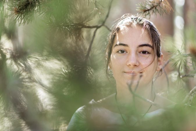 Brown eyes female seen behind green tree branches with selective focus