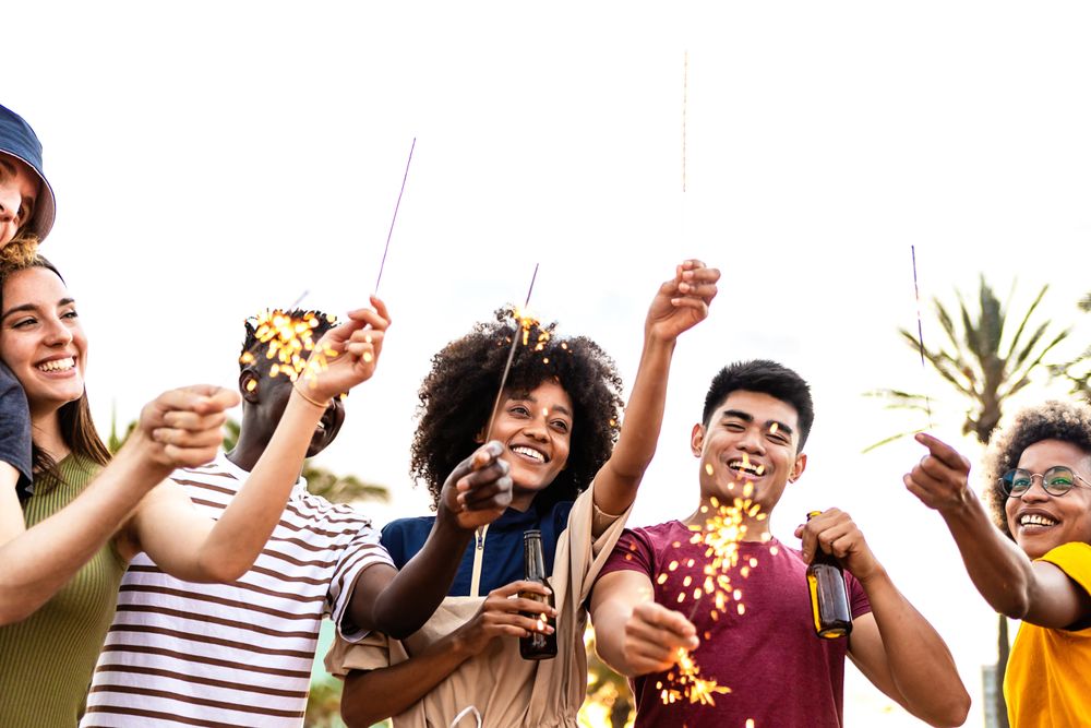 Happy multi-ethnic friends and with sparklers and beer outside