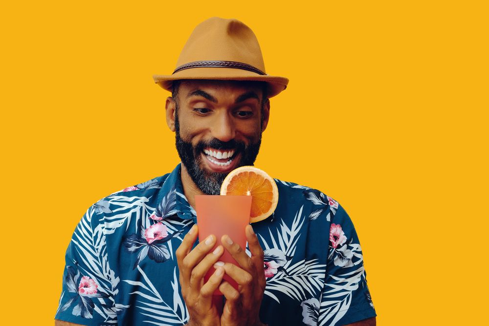 Male wearing colorful shirt and looking appreciatively with cocktail with yellow background
