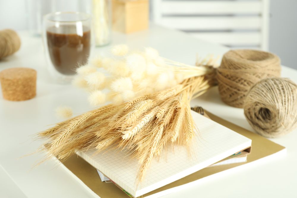 Table of arts and crafts supplies in bright home crafting room, with dried flowers on notebook