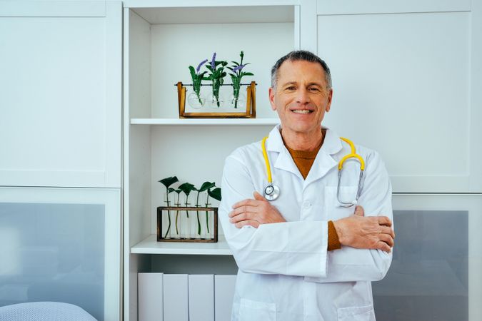 Mature doctor standing in office with arms crossed and smiling