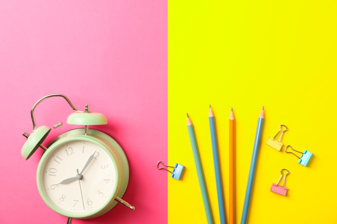 Composition with alarm clock, pencils and clips on two tone background, space for text
