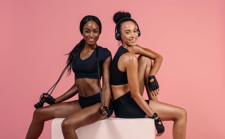 Two female friends sitting on box with skipping rope and smiling