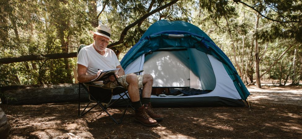 Mature man writing a book at campsite