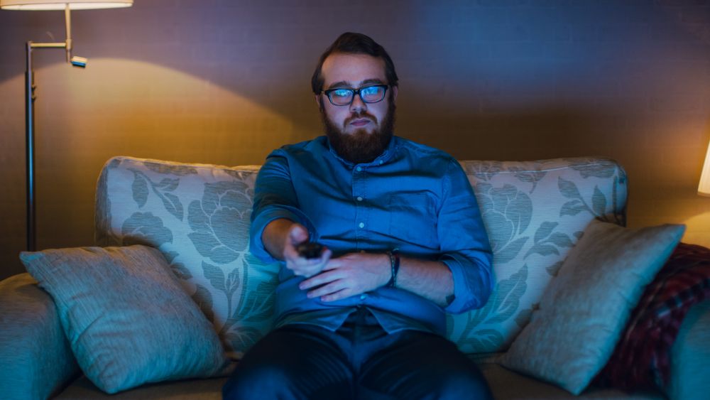 Portrait Shot of a Man Sitting on a Sofa in His Living Room, Eating Popcorn and Watching TV.