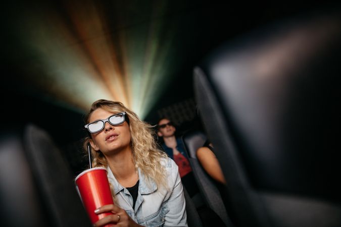 Young woman with cold drink and 3D glasses watching movie in theater