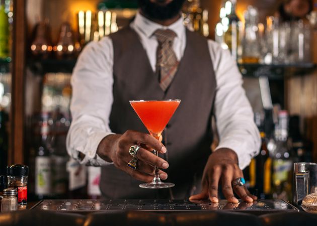 Cutout of a Black bartender offering a cocktail served in a martini glass in a traditional cocktail bar