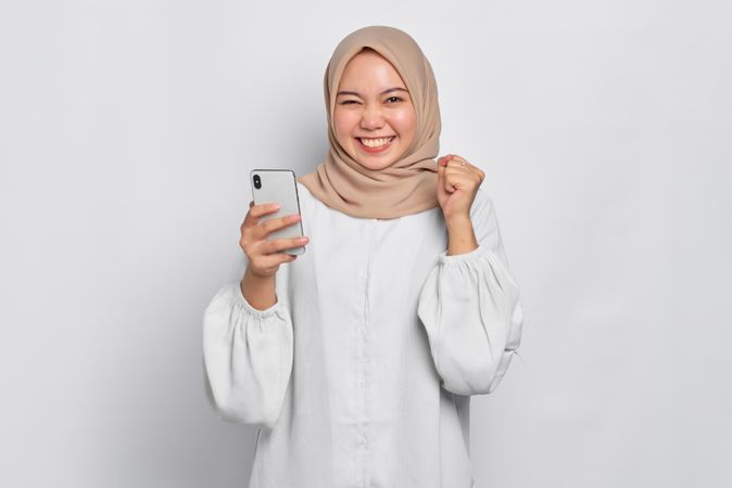 Asian female in headscarf looking excited like she won something while holding cell phone