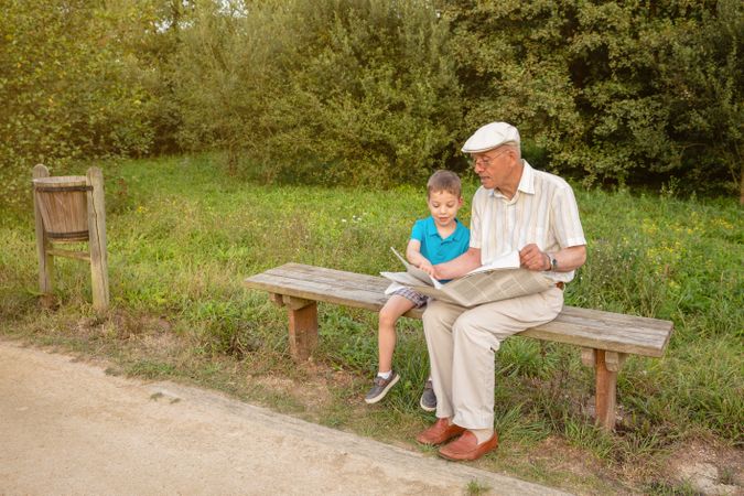 Older man and male child reading a newspaper outdoors