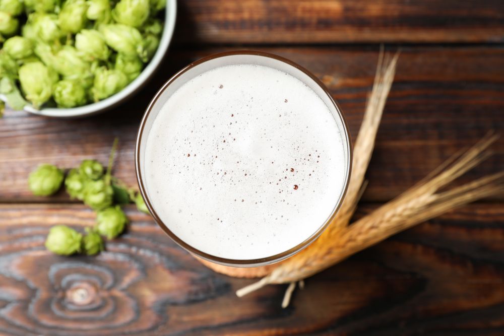 Mug with beer, spikelets and hop on wooden table, top view