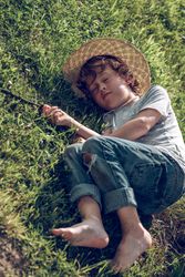 Adorable preteen boy napping on grass in sunny day