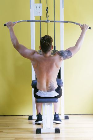 Back of tattooed male exercising his arms on weight machine