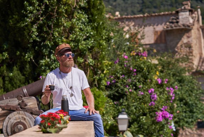 Smiling male tourist in sunglasses drinking tea from thermos
