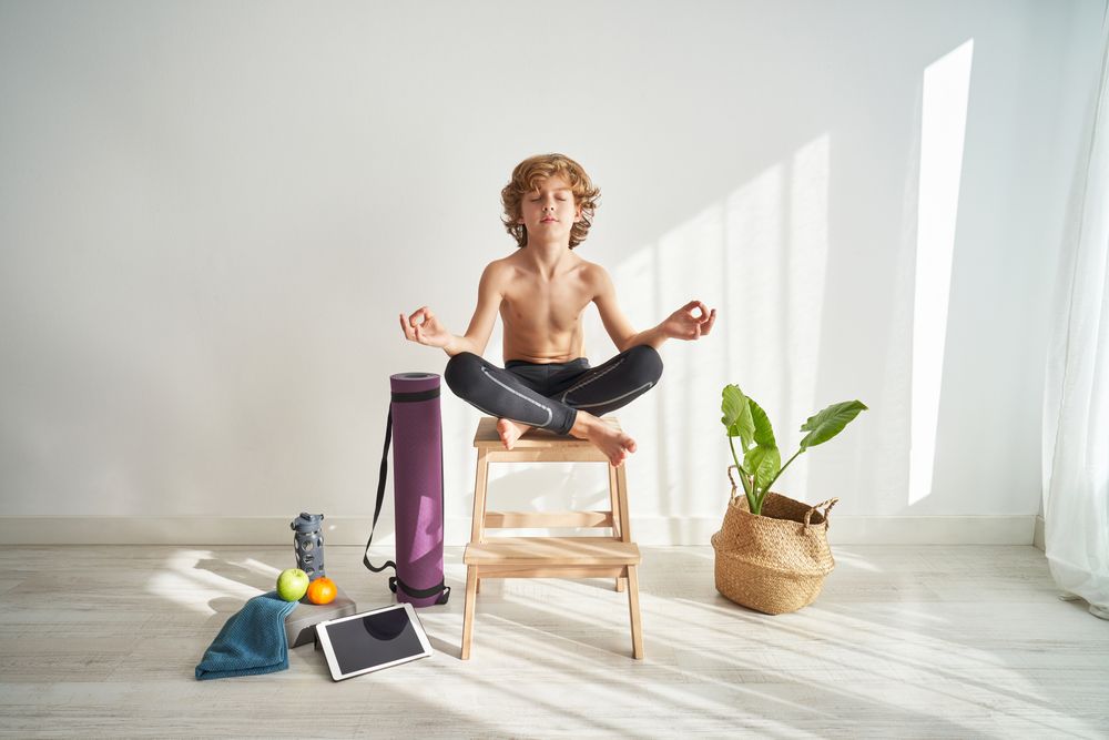 Concentrated boy meditating in Lotus pose on wooden stool