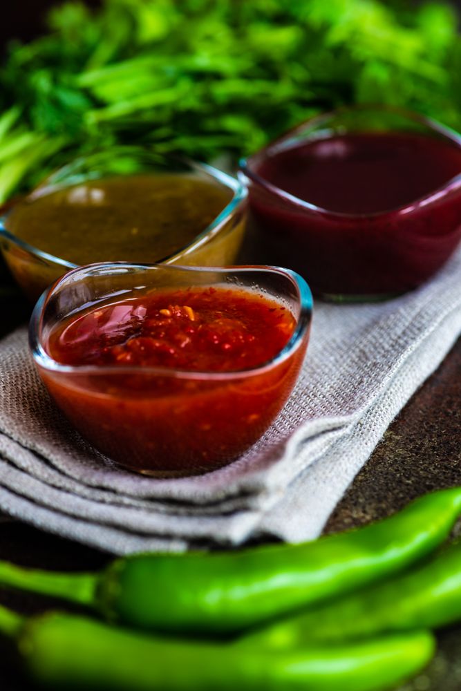 Close up of Georgian sauces tomato satsebeli, yellow and red tkemali with ingredients on stone background with copy space