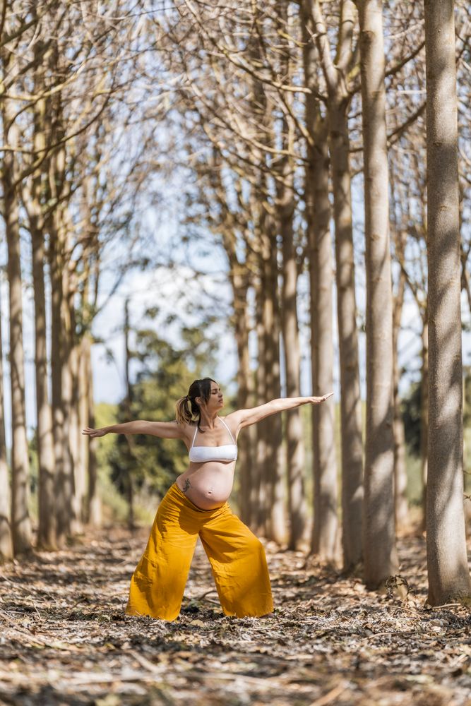 Concentrated adult expectant mother practicing yoga in park