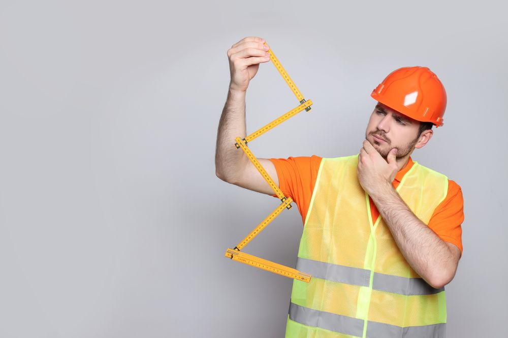 Engineer in helmet with ruler on gray background, space for text