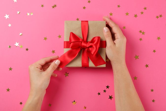 Young woman holding gift box on pink background, space for text