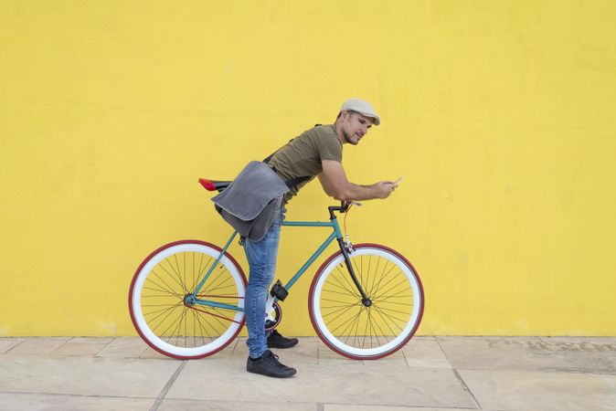 Male in hat and sunglasses looking up from phone while sitting on colorful bicycle