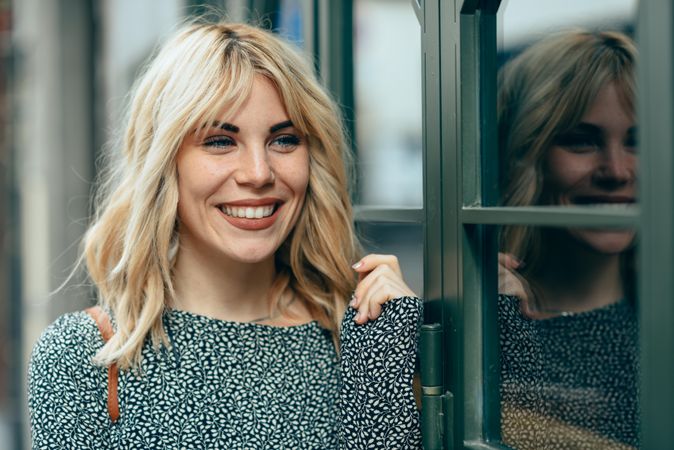 Portrait of blonde female wearing standing next to windows outside