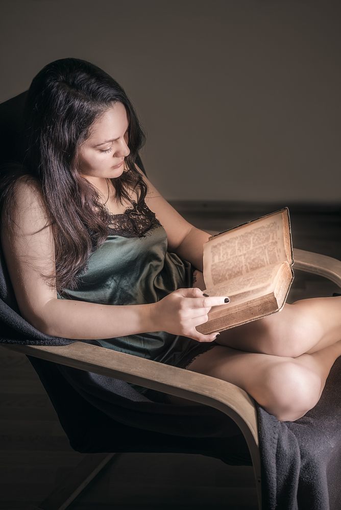 Woman reading in an armchair by a window with natural light