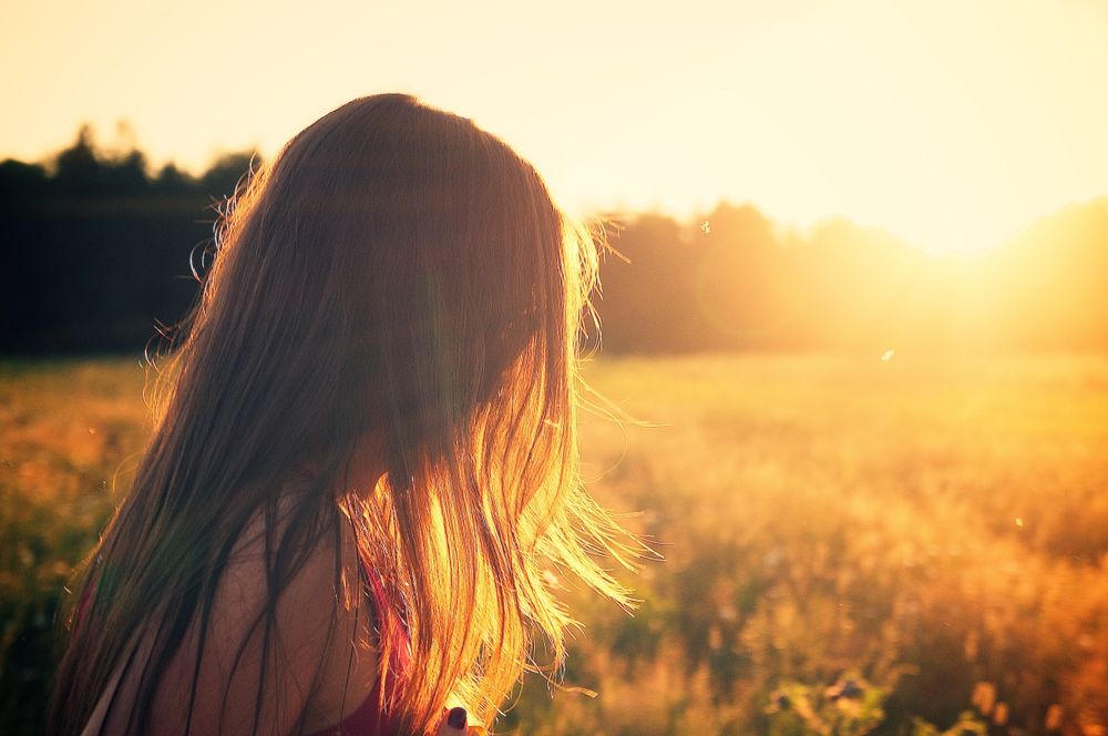 Female person standing near yellow meadow at sunset