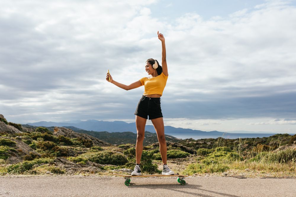 Smiling woman on longboard raising hand and taking selfie