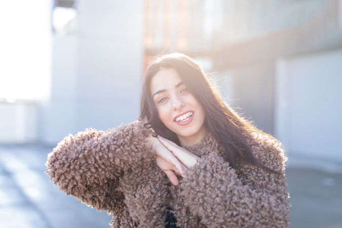 Cheerful woman wrapping in coat on street