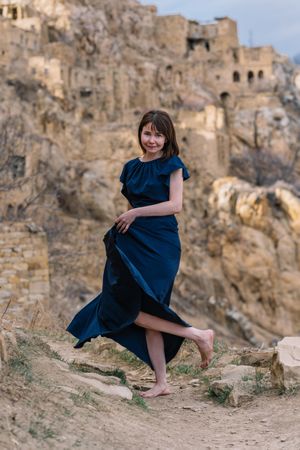 Mature woman in long blue dress standing in natural landscape