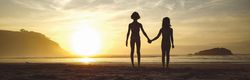 Silhouettes of two girls holding her hands in the beach at sunset