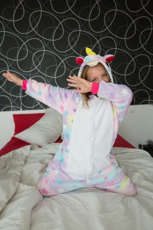 Cheerful girl in unicorn pajama having fun on bed