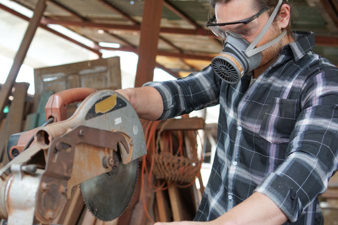 Male carpenter using electric circular saw cutting wood board in workshop