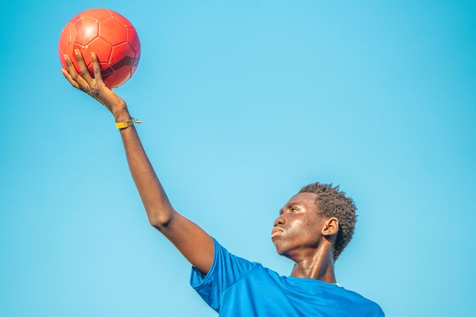 Black teenager with football ball against sky