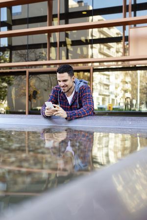 Man with smartphone by city fountain, vertical composition