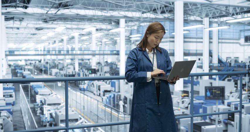 Electronics Manufacturing Technician Working on a Laptop Computer at a Factory Space. Asian Female Specialist Developing, Maintaining, Fine-Tuning Programs for Machine Production and Assembly