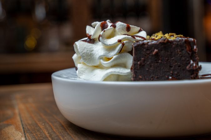 Chocolate brownie slice with whipped cream and chocolate sauce on a plate