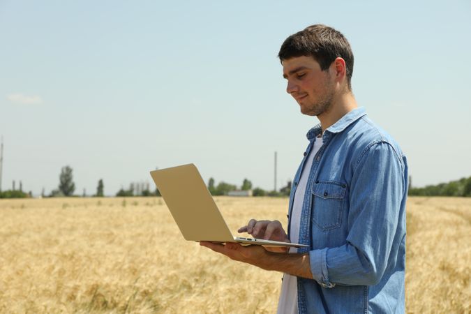 Young man with laptop in barley field. Agriculture business. Farming
