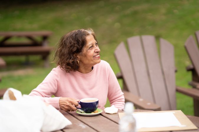 Older Indian woman sitting outside sipping tea