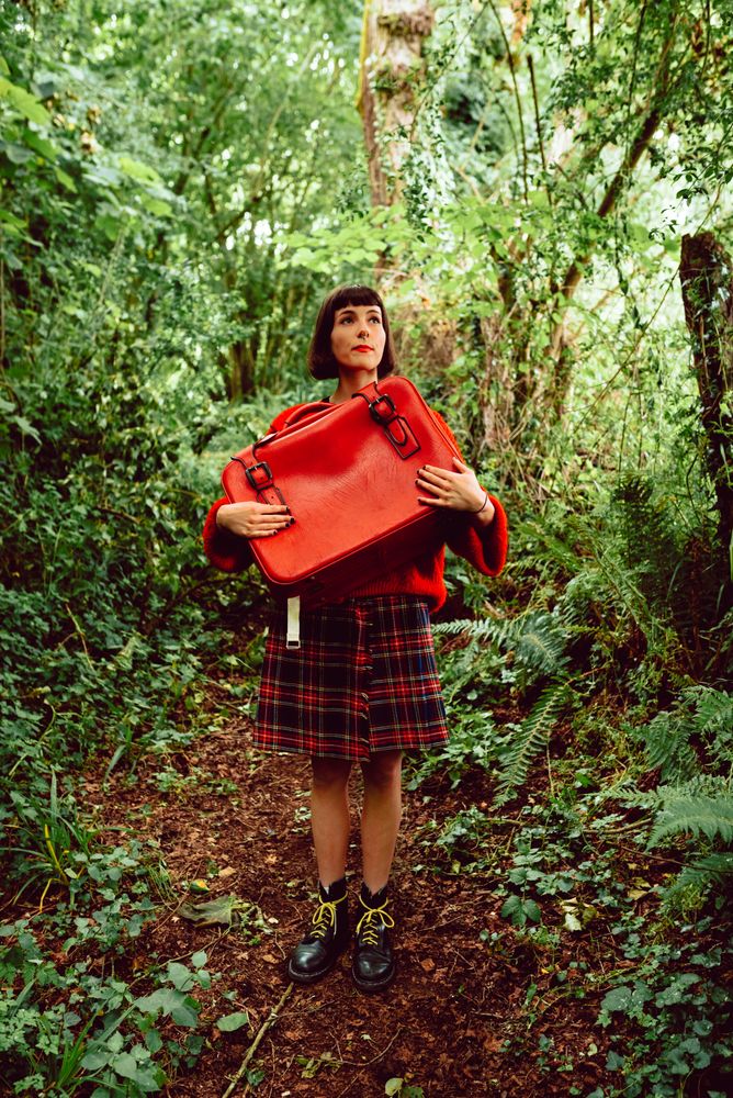 Woman in red with big red suitcase in forest