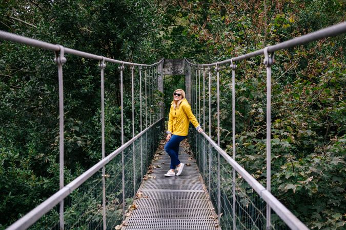 Cheerful female tourist standing on hanging bridge in summer