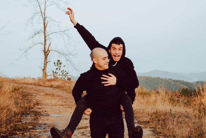 Smiling man holding on back cheerful guy on road on hill