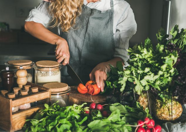 Blonde woman chopping heirloom tomatoes with knife in rustic kitchen