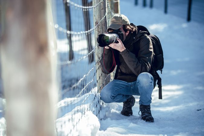 Man taking photo on camera near fence between snow