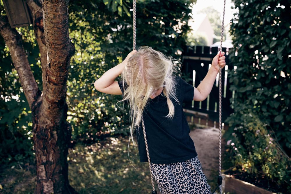 Blonde girl with braided hair looking down while standing on outdoor swing